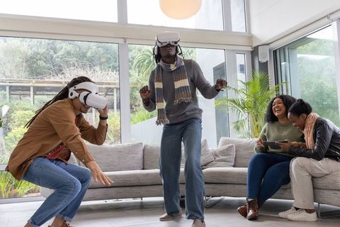 African American friends enjoying virtual reality at home wearing VR headsets and laughing