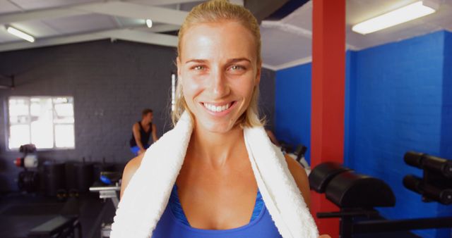 Young woman with towel around neck, smiling after workout session in a gym. Suitable for promoting gym memberships, fitness programs, healthy lifestyle content, workout gear advertisements, and positive wellness messaging.