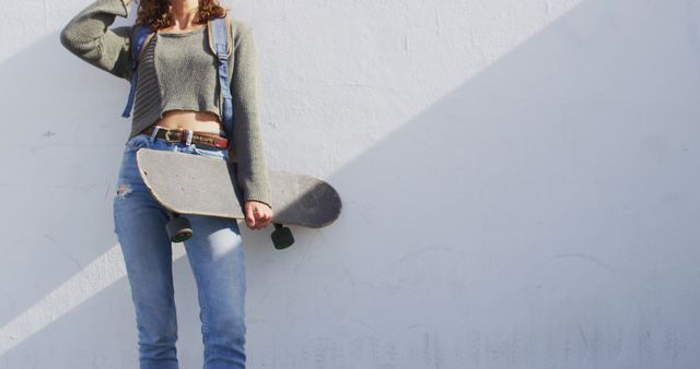 Happy biracial woman holding skateboard, leaning against wall smiling in the sun - Download Free Stock Photos Pikwizard.com
