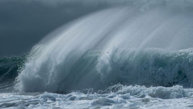 Towering breaking ocean wave curling and spraying mist over windswept turbulent shoreline