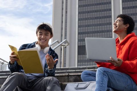 Two College Friends Studying and Laughing on Urban Campus Steps with Laptop and Notebook