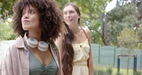 Diverse women walking in park wearing summer outfits and headphones outdoor lifestyle