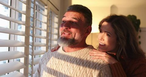 Middle-Aged Couple Sharing Warm Sunlit Moment by Window Shutters, Cozy Home Romance