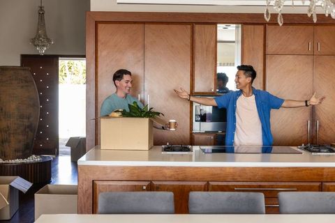 Diverse male friends unpacking boxes and celebrating move-in at modern wood kitchen island