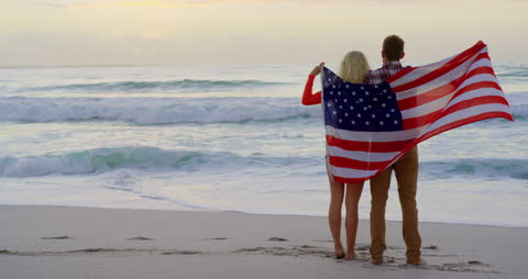 Couple Embracing Under U.S. Flag on Beach