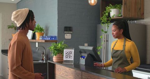 African american customer tapping phone for qr payment at modern cozy cafe counter