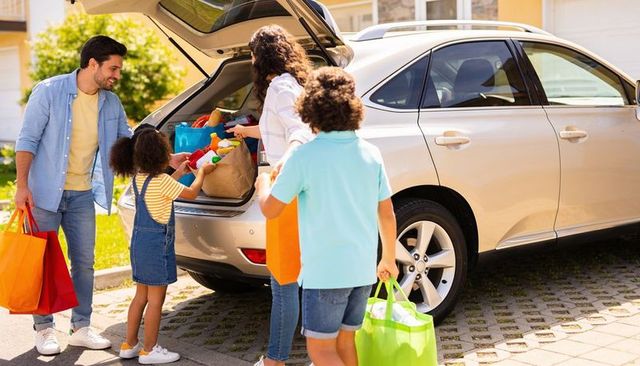 Happy family unloading groceries from suv trunk using reusable bags in suburban driveway
