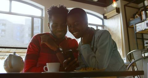 Couple Smiling at Smartphone While Relaxing in Cafe