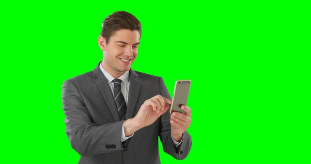 Businessman in a gray suit smiling while using smartphone against a green screen background. Ideal for use in corporate, technology, advertising, and communication contexts, or for easy background replacement.