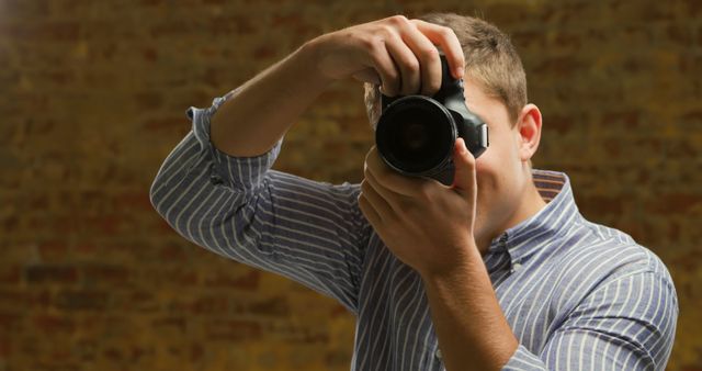 Portrait of caucasian man taking photo with camera in front of brick wall - Download Free Stock Photos Pikwizard.com