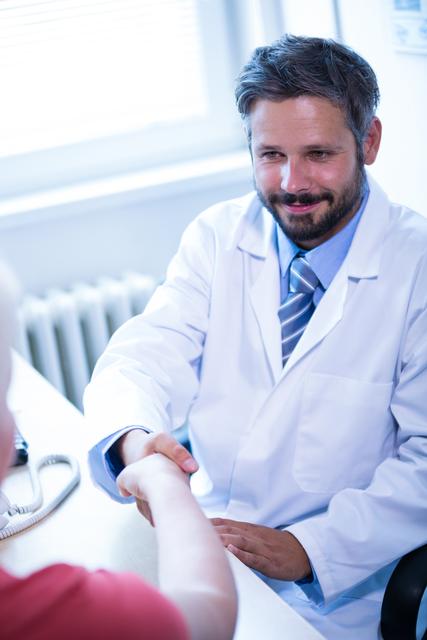 Doctor shaking hands with patient in medical office, indicating trust and professional relationship. Ideal for healthcare, medical services, patient care, and professional consultation themes.