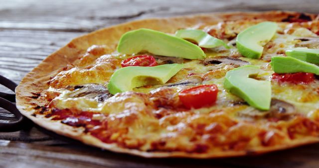 Closeup of thin-crust pizza topped with melted cheese, avocado slices, mushrooms, and cherry tomatoes. Ideal for use in food blogs, recipe websites, and health-focused meal promotions. Perfect for restaurant menus, social media posts about healthy eating, or culinary magazines showcasing gourmet pizza options.