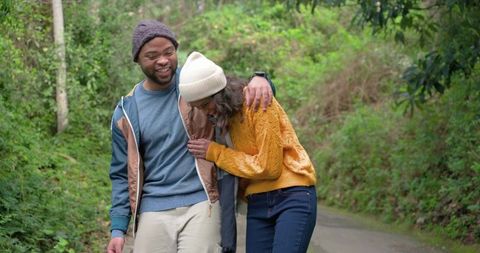 Smiling couple walking woodland trail wearing knit beanies and mustard sweater
