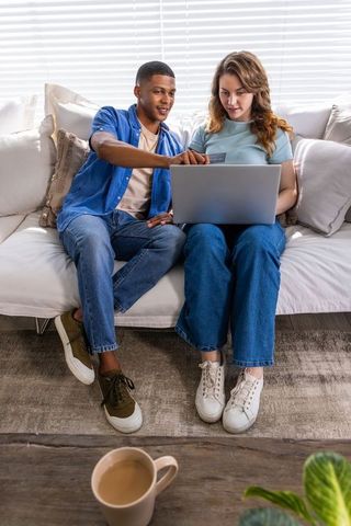 Mixed-race couple shopping online on sofa using laptop and credit card
