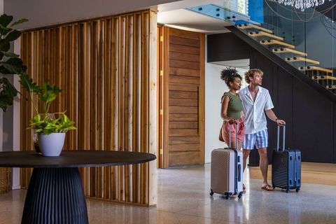 Young couple arriving at modern hotel lobby pulling rolling suitcases and looking around