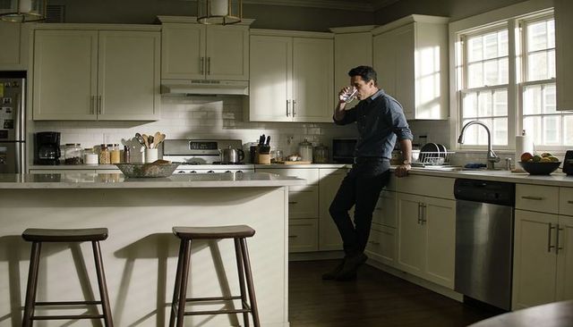 Man leaning on kitchen counter drinking water in sunlit modern transitional interior
