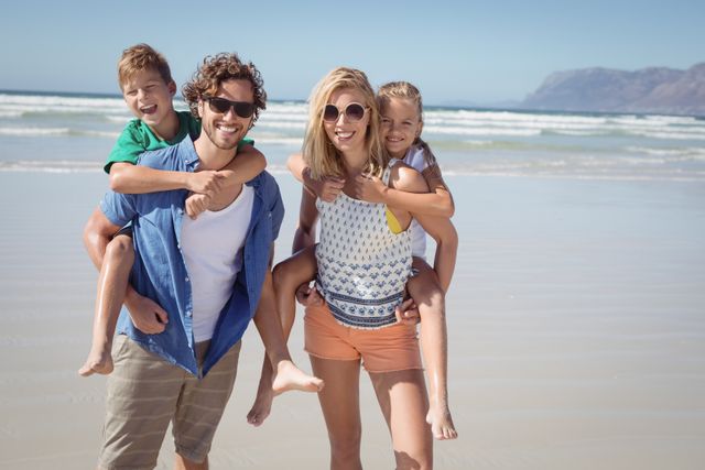 Portrait of smiling parents piggybacking their children at beach during sunny day