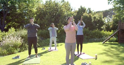 Group practicing standing meditation on sunlit lawn with yoga mats and sneakers
