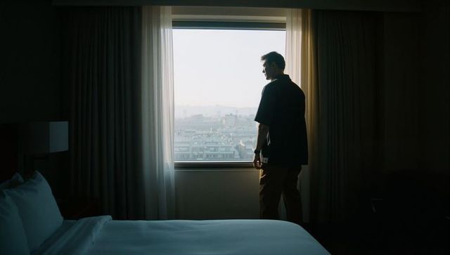 Standing silhouette in hotel room gazing at urban skyline morning light moody contemplative