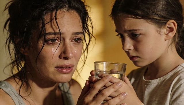 Tearful mother comforting daughter holding glass of water, intimate caring family moment