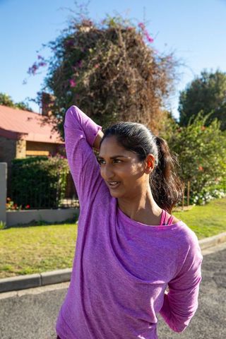 Woman in activewear stretching outdoors on sunny day