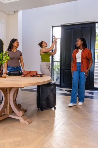 Female friends examining black front door in modern foyer with luggage and round table