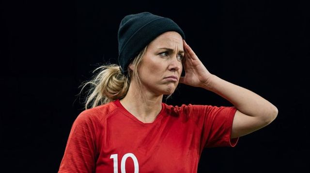 Frustrated female athlete touching temple wearing red jersey number 10 and black beanie