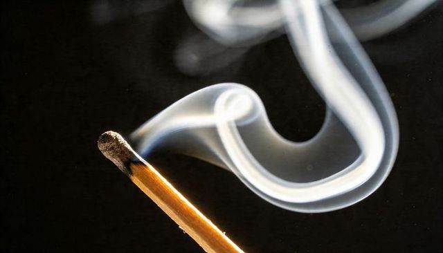 Burning Matchstick Smoking with Curling Smoke and Charred Tip on Dark Contrast Background
