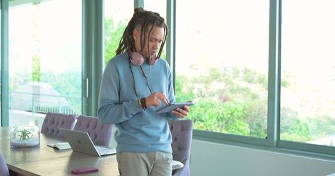 African american man using tablet in bright modern home office with laptop and headphones