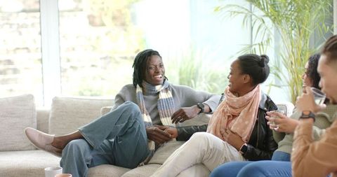 Diverse friends laughing and chatting on cozy sectional sofa during bright daytime hangout
