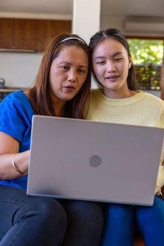 Asian Mother and Daughter Learning Together on Couch with Laptop