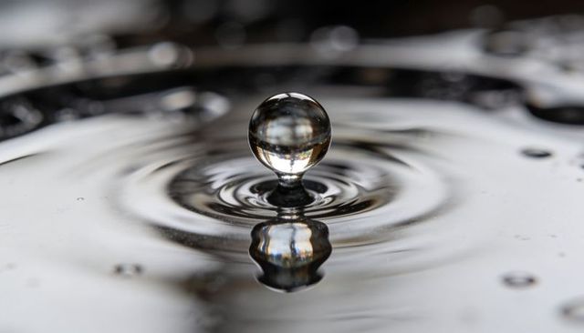 Crystal water droplet rebounding with mirror reflection and ripples monochrome macro