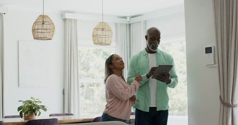 African american couple using tablet to control smart home in modern dining room