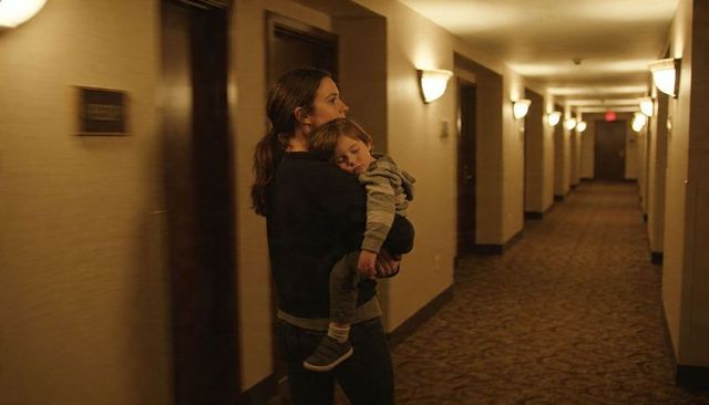 Mother carrying sleeping toddler down dim hotel corridor, late night travel and caregiving