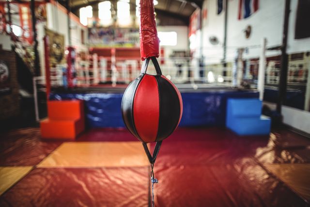 Speed boxing ball hanging in a fitness studio, with a boxing ring in the background. Ideal for use in articles or advertisements related to fitness, boxing training, gym equipment, and athletic workouts. Perfect for promoting boxing classes, gym memberships, and fitness programs.