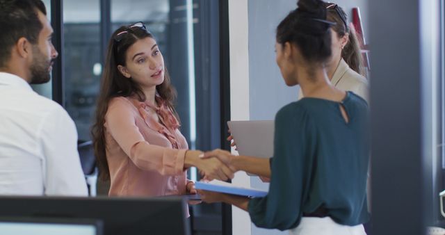 Two diverse businesswomen standing shaking hands during meeting with colleagues. independent creative business in a modern office.
