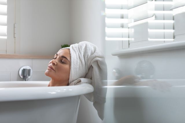 Serene and peaceful woman with towel wrapped around her head enjoying a relaxing bath at home. Perfect for content related to self-care, relaxation, home lifestyle, wellness routines, and personal pampering.