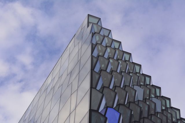 Architectural marvel with a striking geometric design featuring numerous glass panels against a clear blue sky. Ideal for use in real estate, urban development presentations, architecture portfolios, and design inspiration.