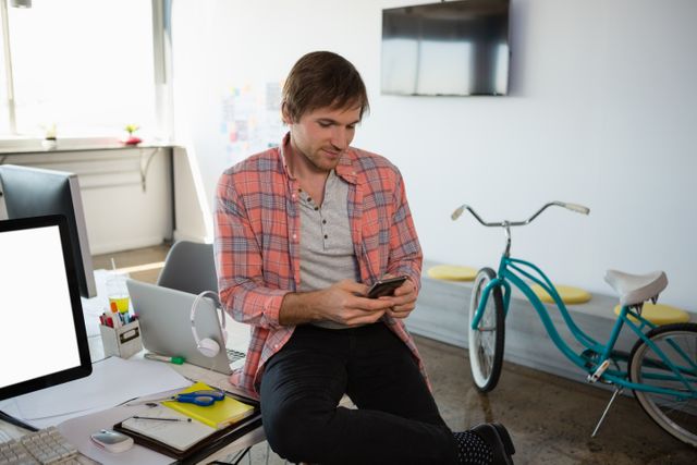 Young businessman using phone while sitting on desk at office