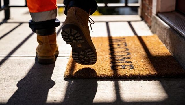 Construction worker stepping onto porch with rugged boots and welcome mat in sunlight