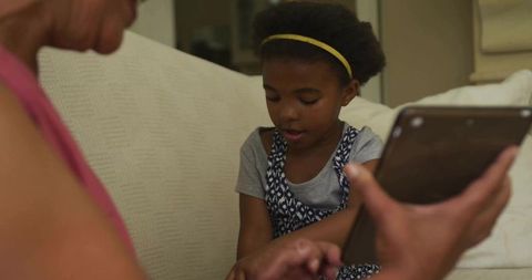 Grandmother with Tablet Showing Technology to Curious Granddaughter on Couch