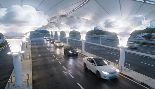 Illuminated canopy driveway with moving cars on wet road at dusk