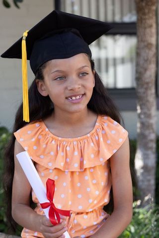 Young graduate wearing mortarboard holding diploma with red ribbon orange polka dot dress