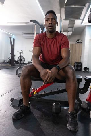 Focused african american man resting on bench after intense workout in modern gym