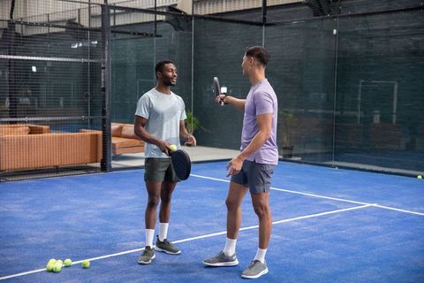 Two friends practicing padel on blue court wearing casual sportswear and holding rackets