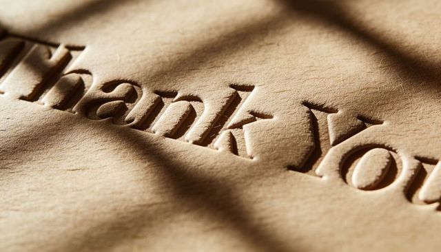 Showing debossed thank you on kraft paper with warm blind shadows macro closeup