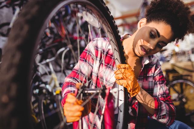 Female bicycle mechanic wearing orange gloves repairing bike in workshop, hands using tools. Suitable for concepts related to skilled labor, bicycle maintenance, repair services, and women in trades.