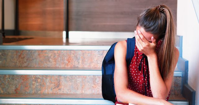 A young woman exhibits signs of distress while seated on steps, hand covering her face. - Download Free Stock Photos Pikwizard.com