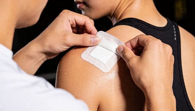 Applying Adhesive Medical Patch to Sweaty Shoulder During Workout