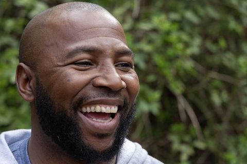 African american man laughing in garden wearing light gray hoodie with open smile